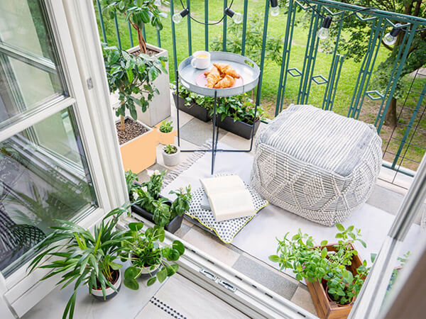 A cozy balcony decorated with a pouf and side table serving tea and croissants