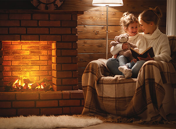 A mom reads a book to her daughter beside the fireplace